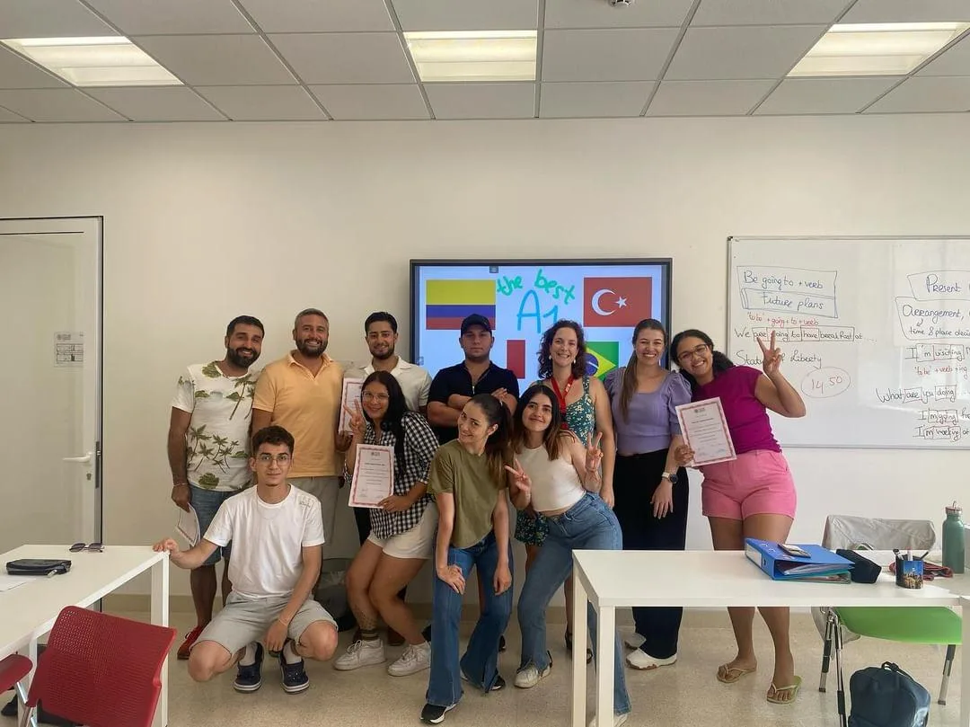 A class with their certificates in front of a screen showing the flags of their home countries