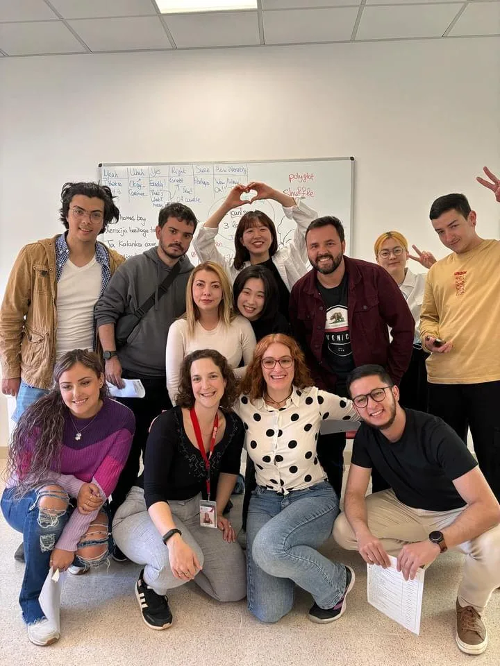 A group of adult students and their teachers posing together in front of a whiteboard