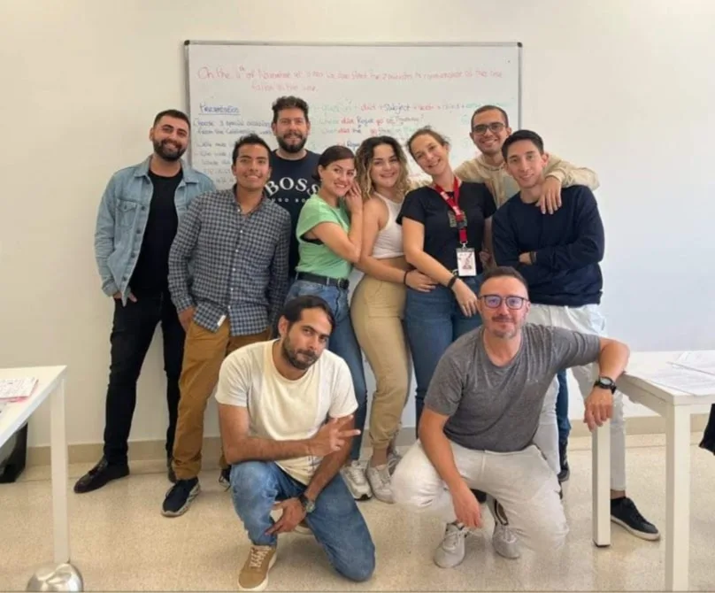 A class of adult students posing together in front of the whiteboard